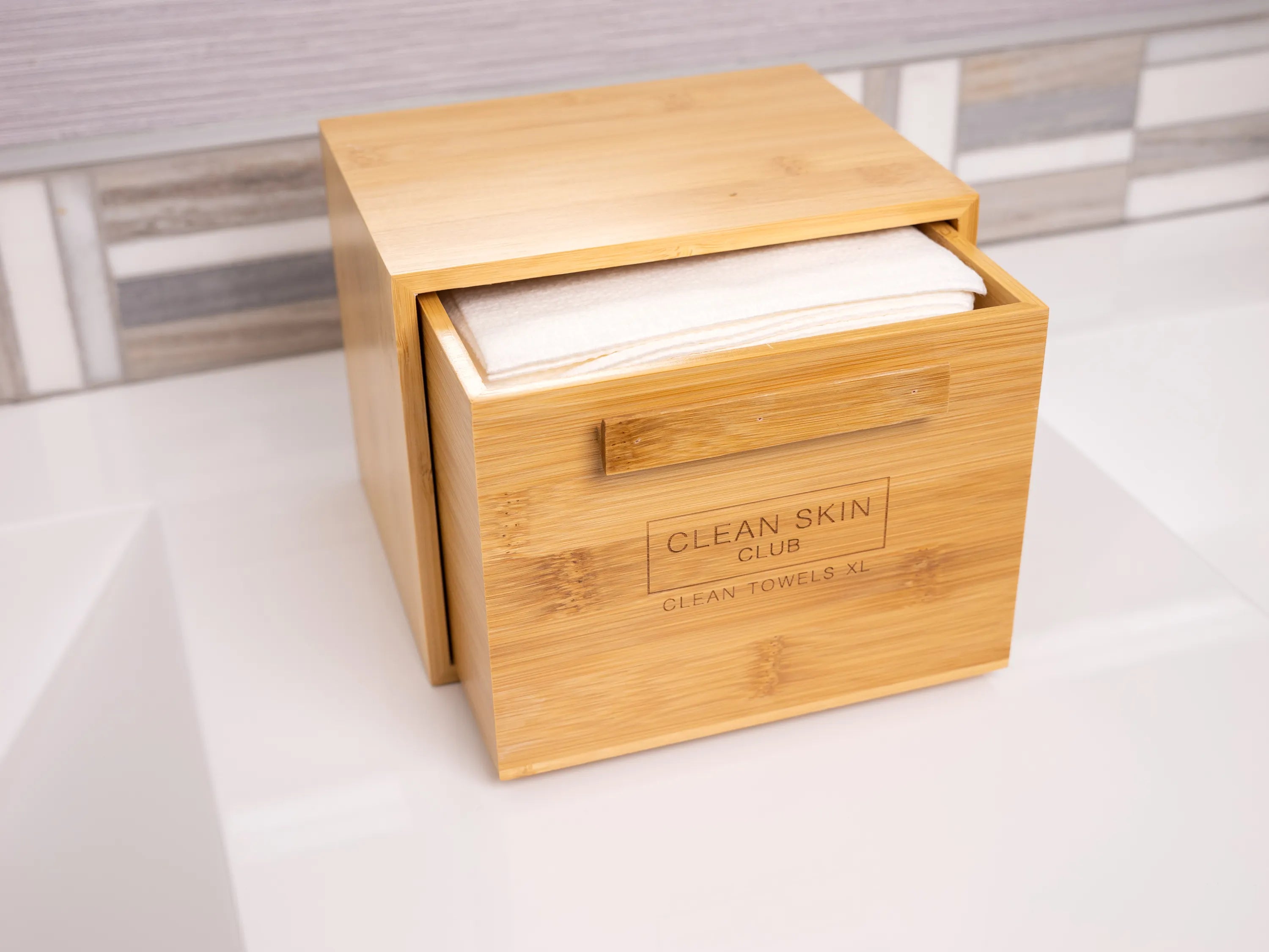 Wooden box with a sliding lid and towels inside, labeled 'Clean Skin Club Clean Towels XL.'
