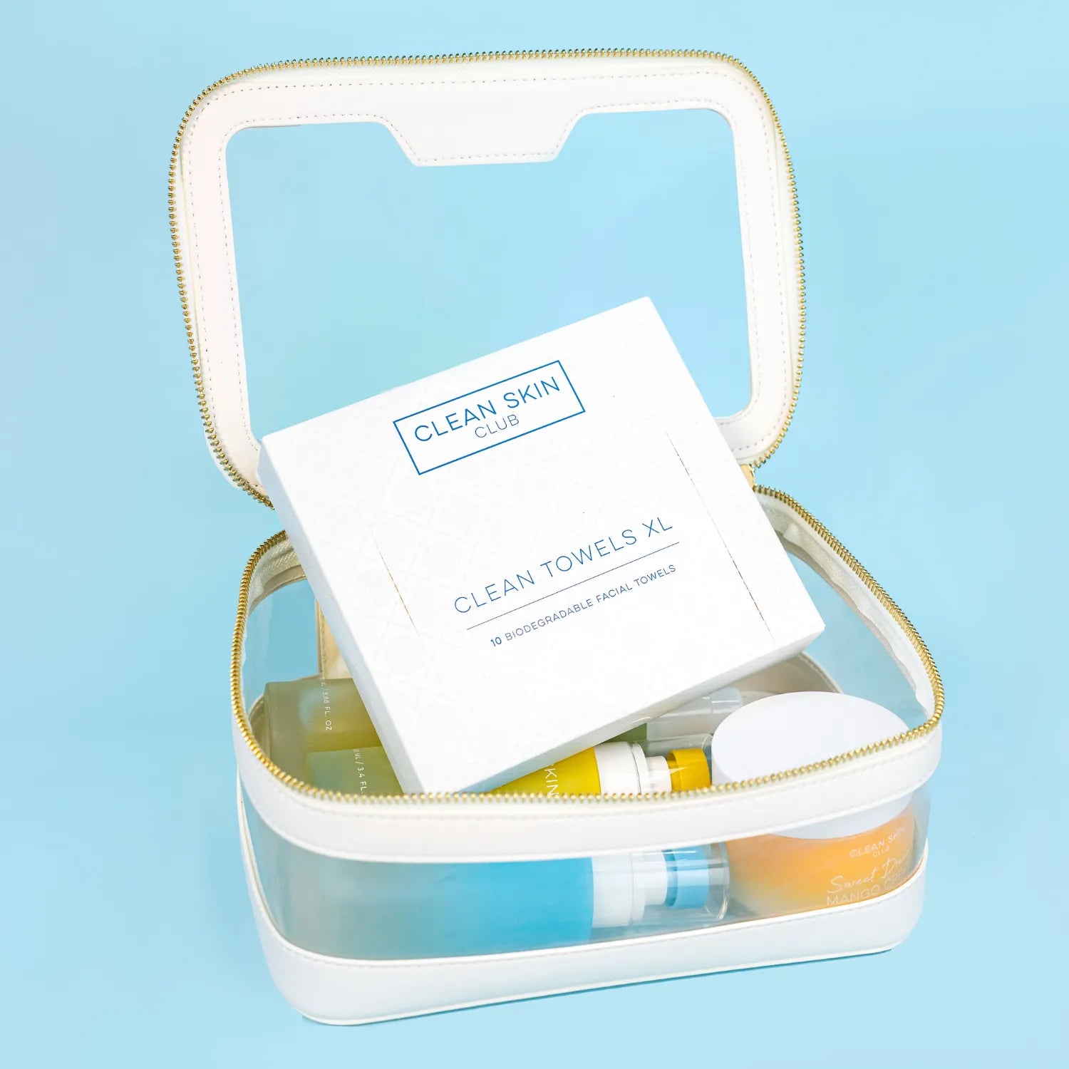 Clear skincare bag with Clean Skin Club towels and bottles against a light blue background.