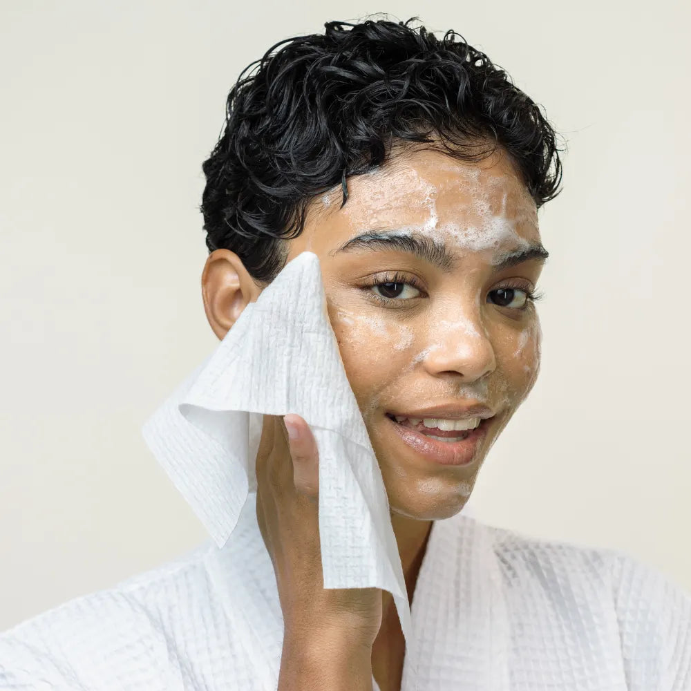 Person cleansing face with foam and using a towel.